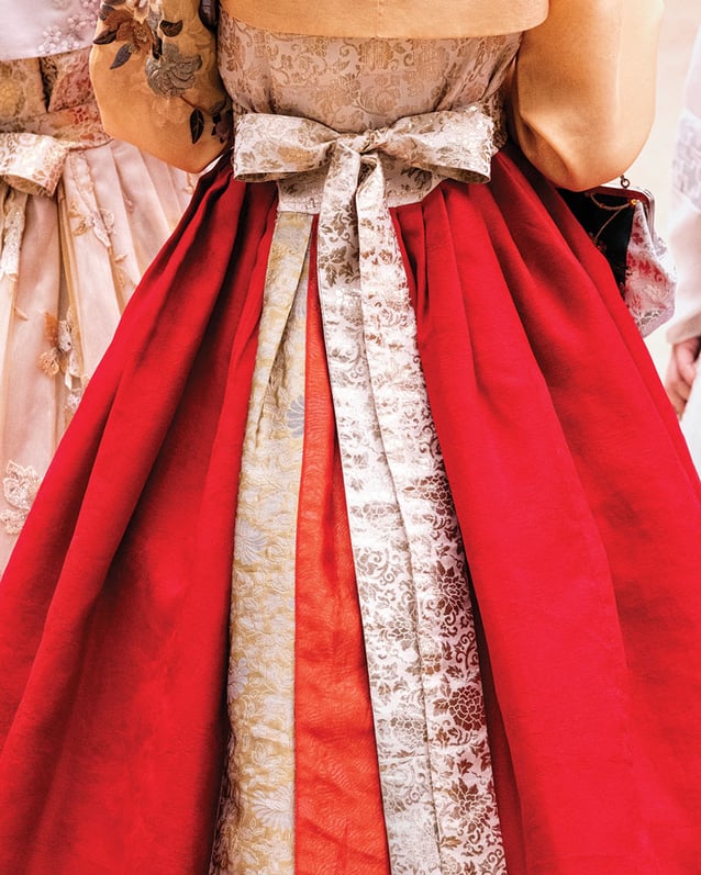 The back of a traditional red hanbok outfit, with patterned fabric panels and a tied bow.