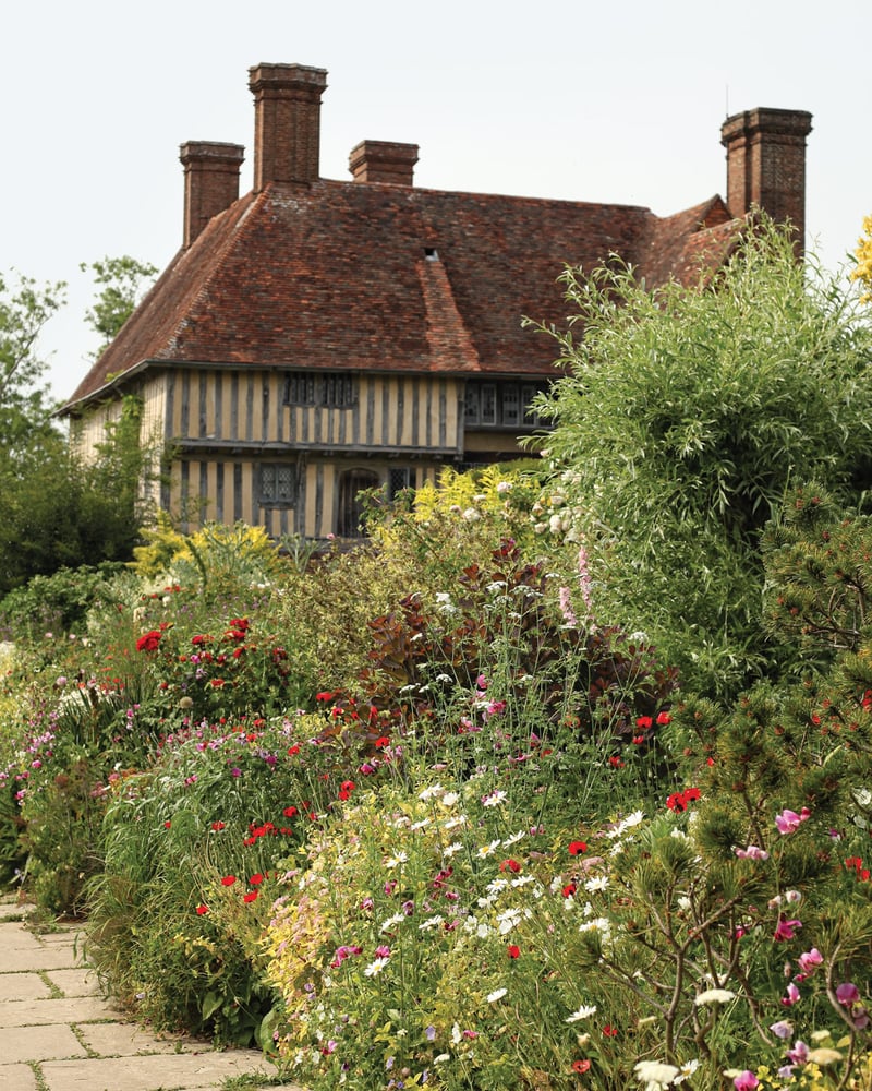 A cottage peeks out from behind a flowering garden.