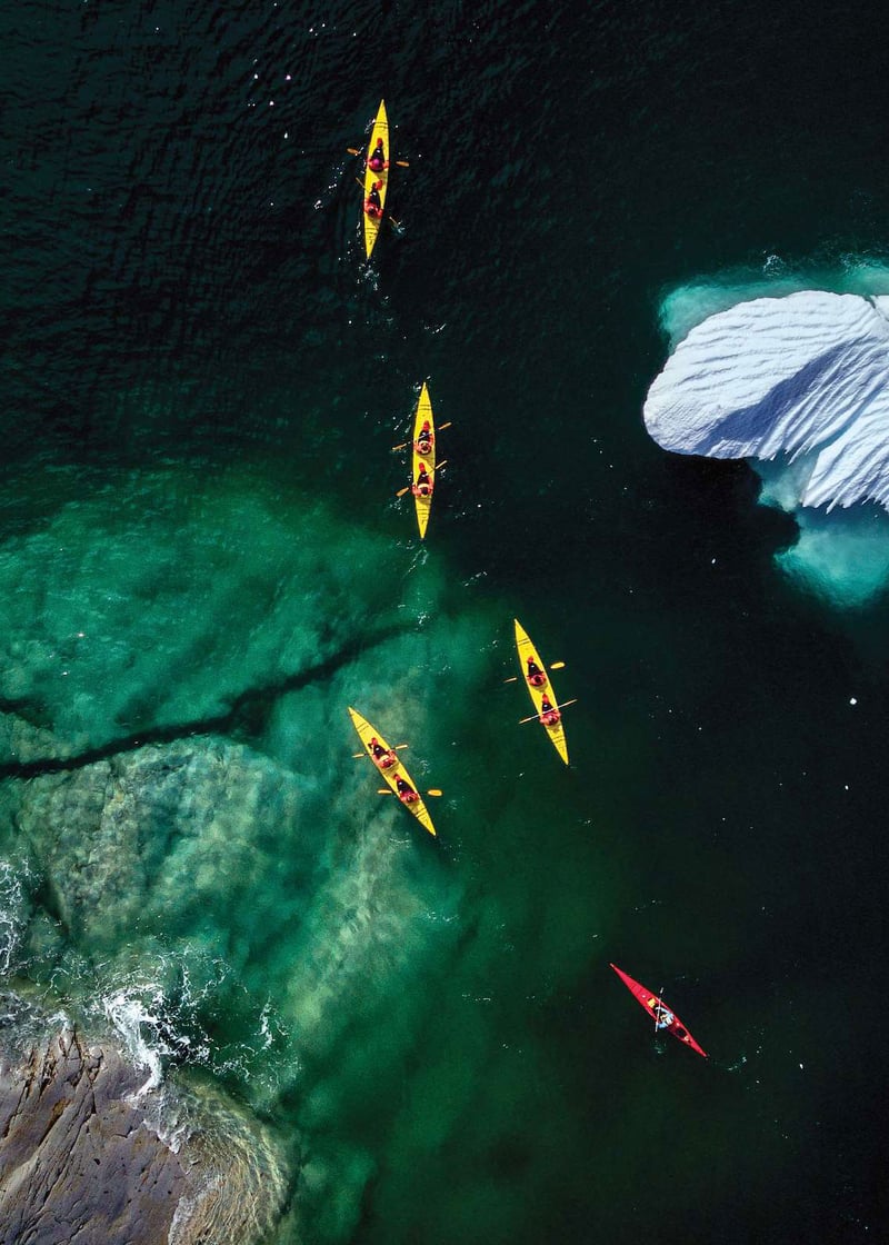 An overhead view of kayakers paddling between boulders and an iceberg in the Nordics.