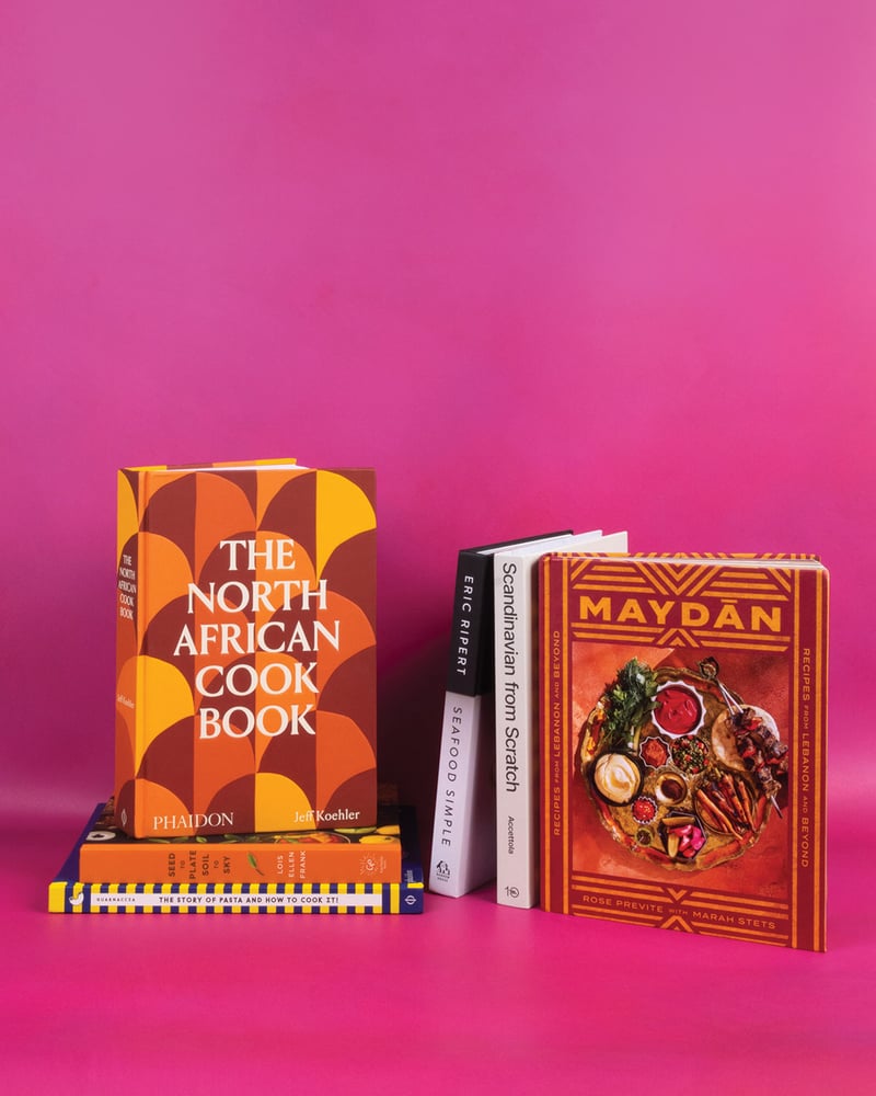 Six cookbooks stacked on a hot-pink background.