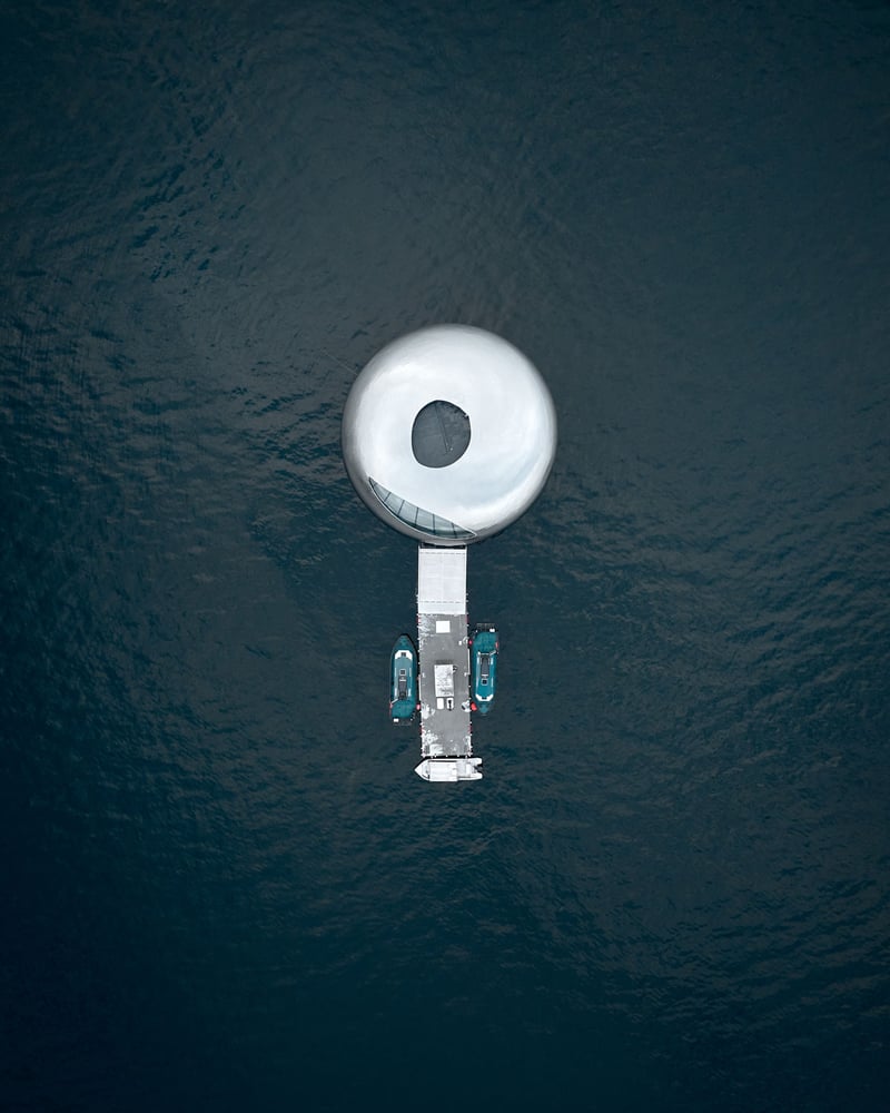 A round silver building and dock, seen from overhead, float in a Norwegian fjord.