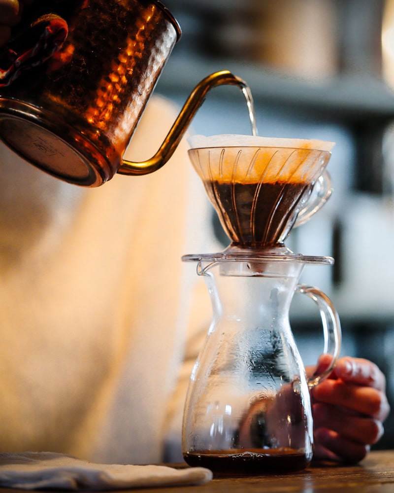 In Kyoto, a café employee pours water from a copper kettle into a pour-over cone.