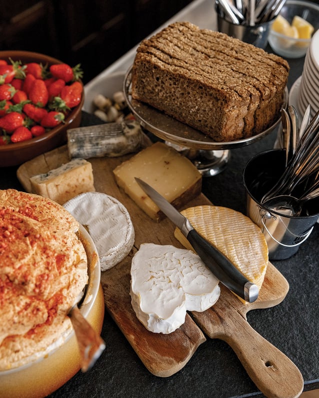 At Le Repaire de Cartouche, a rustic spread of fresh bread, strawberries, and cheeses on a wooden board.