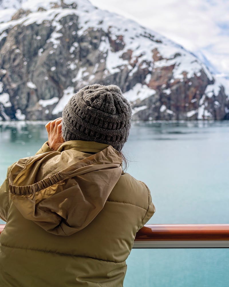 Seen from behind, a woman on a cruise ship looks out at Glacier Bay National Park.