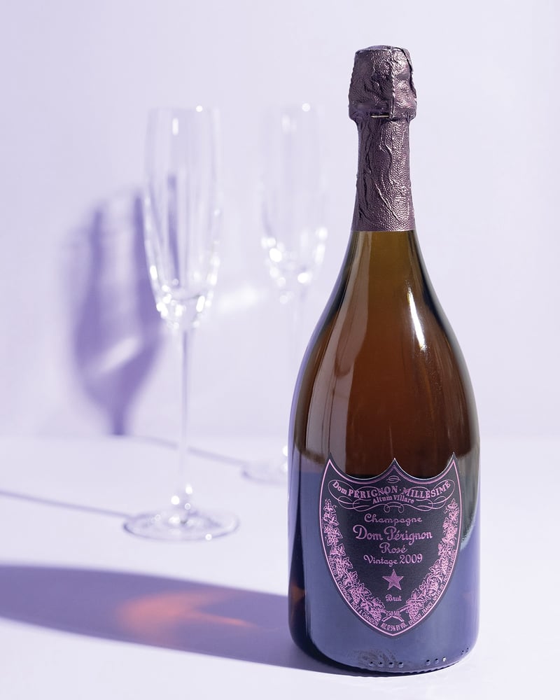 A bottle of Dom Pérignon sits in front of two Champagne glasses on a purple background.