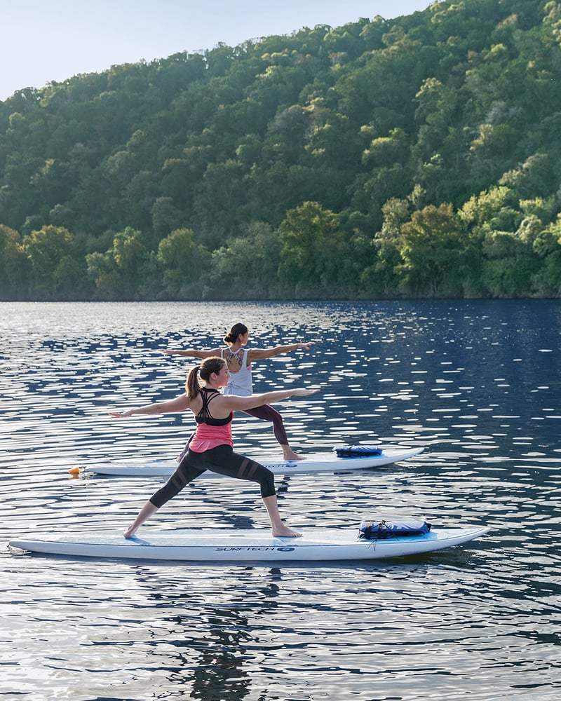 Two women hold yoga poses on stand-up paddleboards floating on Lake Austin.