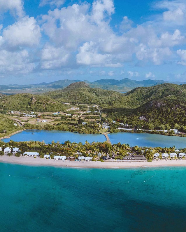 An aerial view of Galley Bay Resort & Spa in Antigua shows its palm‑lined beachfront curving between turquoise Caribbean waters and a tranquil lagoon backed by green hills.