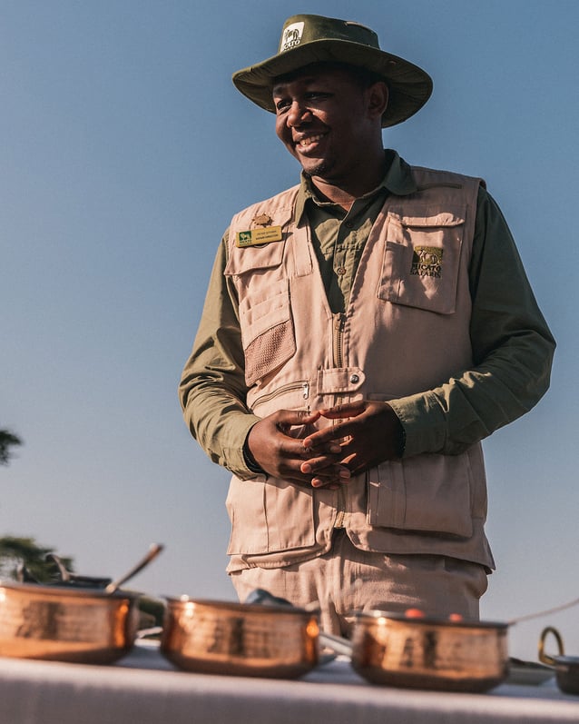 A Micato safari guide stands behind a table set with copper pots.