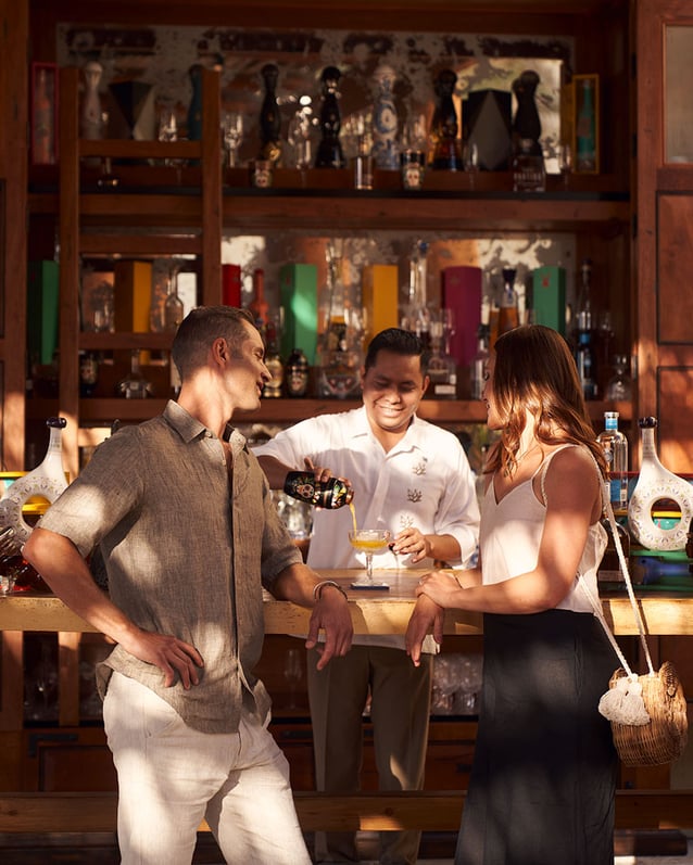 Two guests watch a bartender pour a cocktail at Waldorf Astoria Los Cabos Pedregal’s Agave Study.