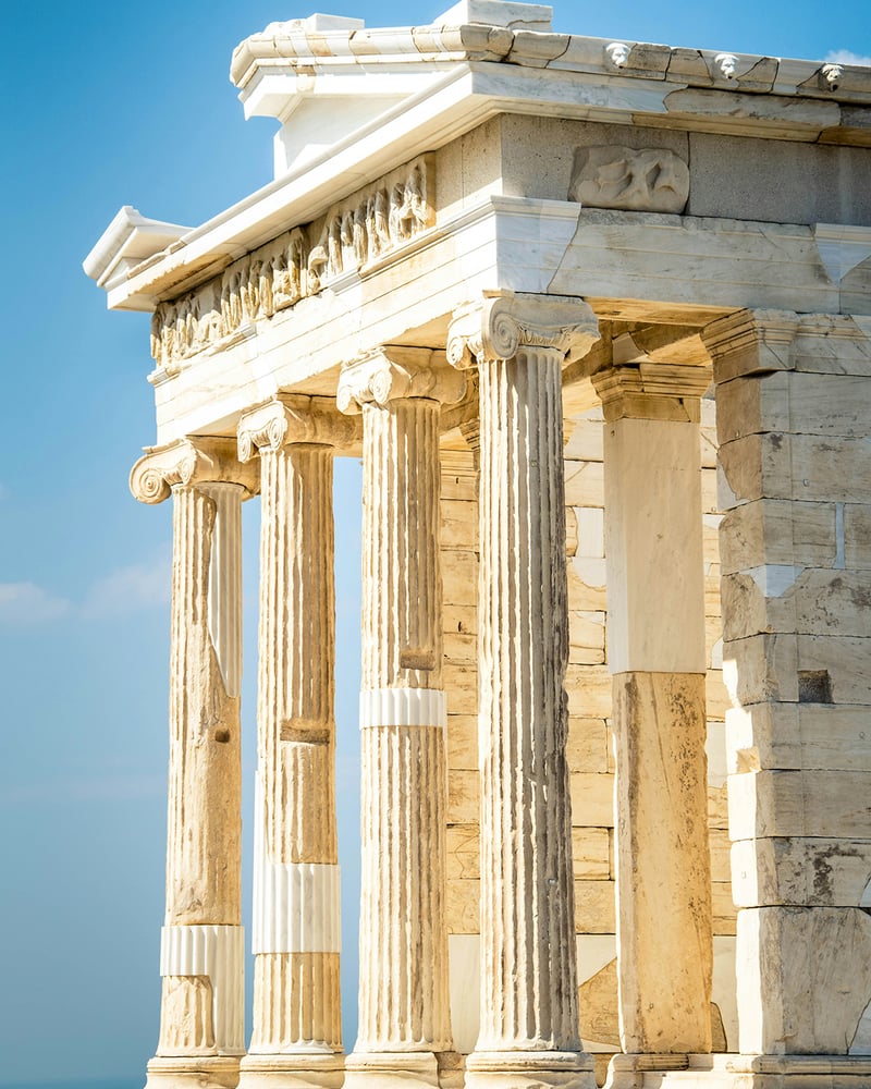 The white marble columns of the Temple of Athena Nike on the Acropolis of Athens against a blue sky.