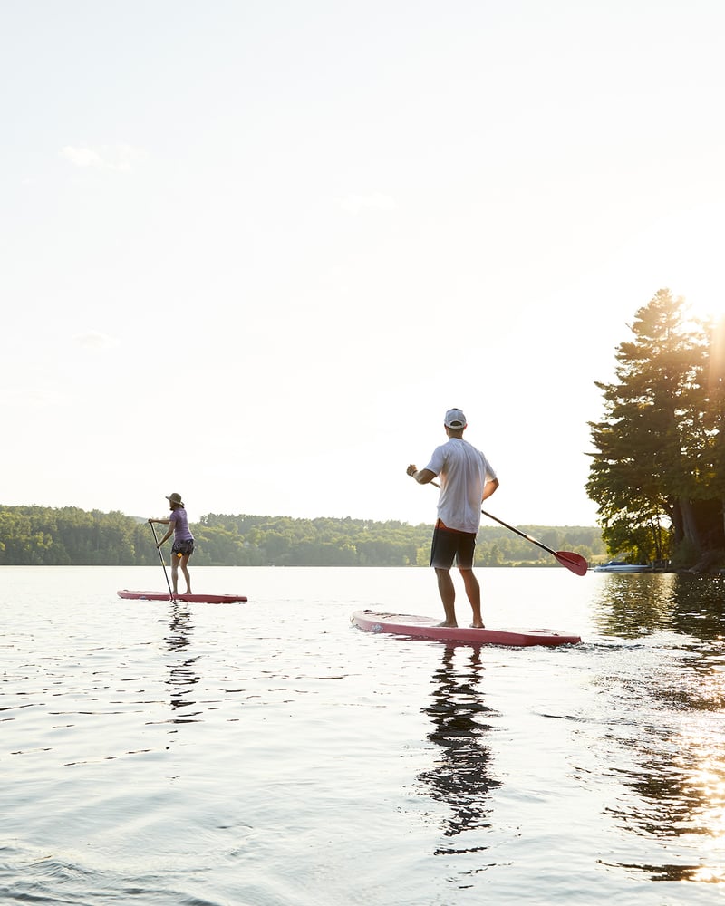 Two people stand-up-paddleboard across Massachusetts’ Laurel Lake at Miraval Berkshires resort.