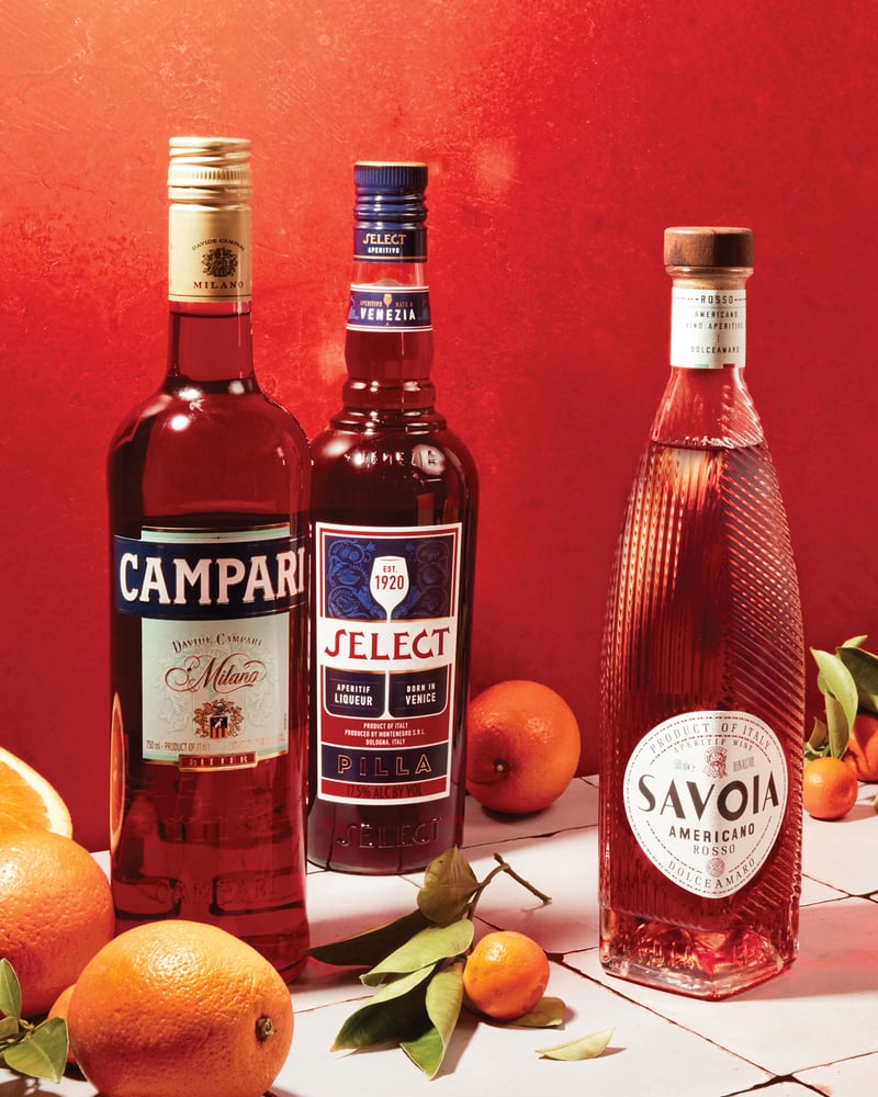 Five aperitivo bottles on a tile countertop, surrounded by fresh oranges.