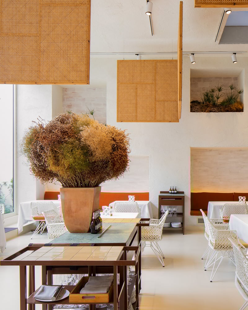 Modern empty tables inside the airy, all-white, high-ceiling interior of Disfratur restaurant in Barcelona.