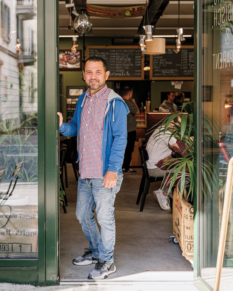 Manolo Gonzalez, owner of Café Tacuba, smiles from the green doorway of his shop.