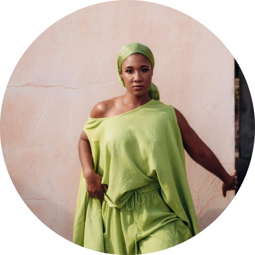 Celene Senhouse, wearing a pale-green headtie and matching outfit, gazes at the camera.