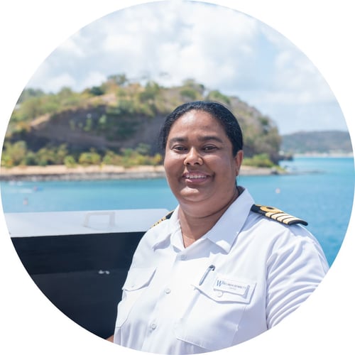 Belinda Bennett, wearing a captain’s uniform, smiles from a Windstar ship near the coast.