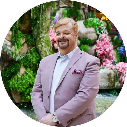 Ed Libby, wearing a lavender suit, smiles while standing in Bellagio’s Conservatory.