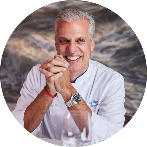 Chef Eric Ripert, wearing chef’s whites and sitting at a restaurant table, smiles and looks off-camera.