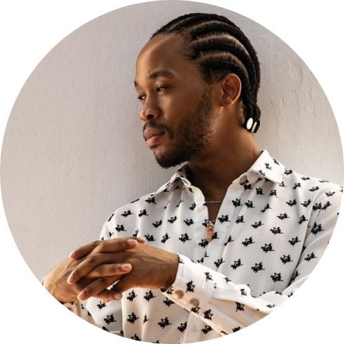 Thebe Magugu, wearing a black-and-white polka-dotted blouse, gazes away from the camera.
