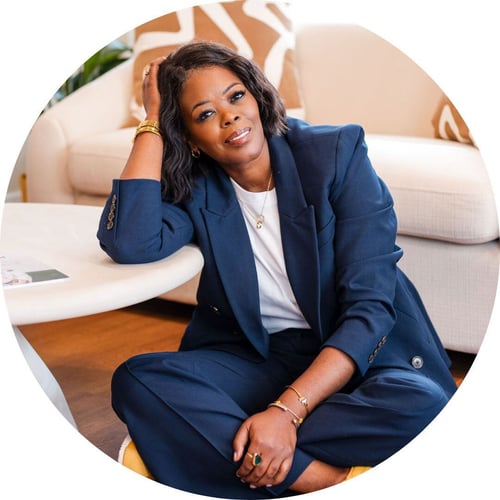 Tina Wells, wearing a navy blazer and gold jewelry, smiles at the camera.