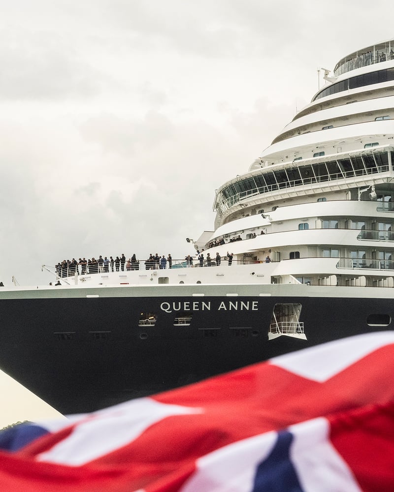 Queen Anne pulls into port as a British flag waves in the foreground.