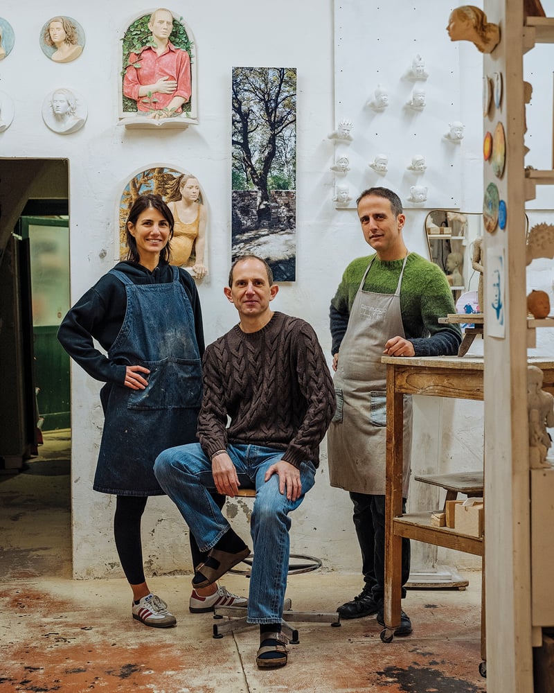 Florentine artists Virginia De Gasperis, Giovanni Garuglieri, and Oliviero Draghi in an art studio. Sculptural figures hang on the wall behind them.
