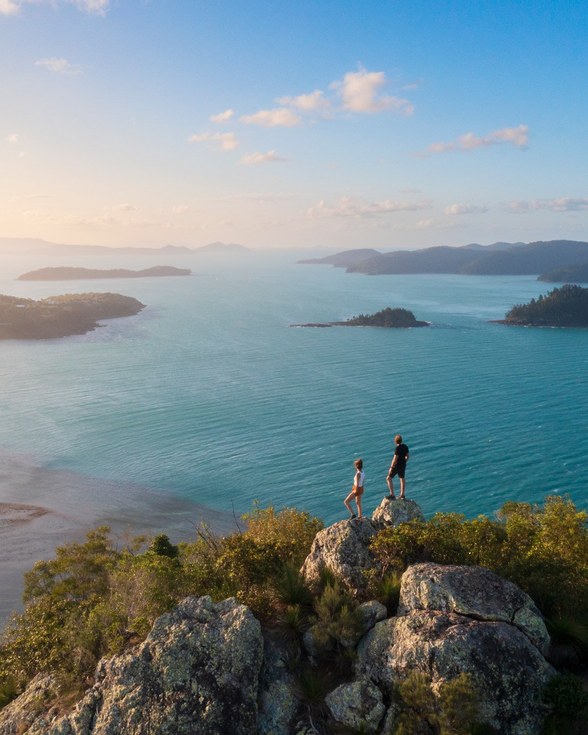 Hikers stand atop rocks on a mountain overlooking the beach.