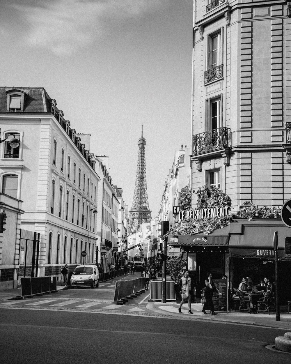 The Eiffel Tower, seen from between apartments and a café on a Paris street.