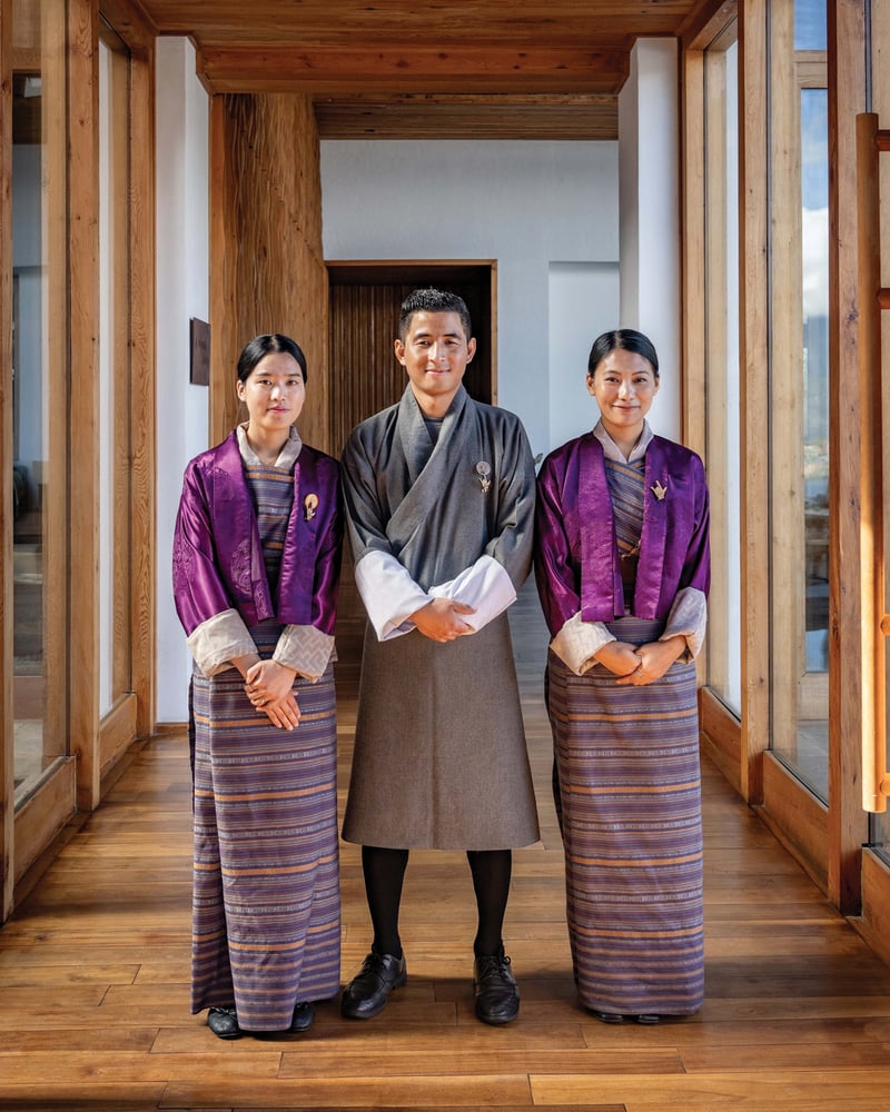 Three staff members at Six Senses Bhutan smile at the camera, wearing traditional dress.