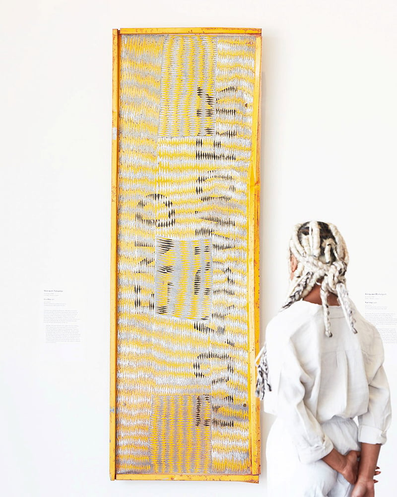 A woman stands with her back to the camera as she looks at a work of art in a gallery.