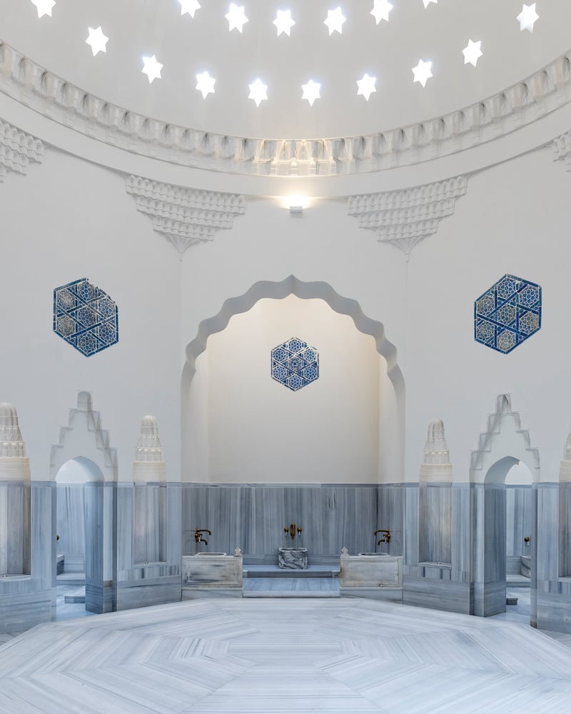 The domed interior of the Zeyrek Cinili Hamam in Istanbul, with gray marble basins, brass faucets, and blue tile mosaics.