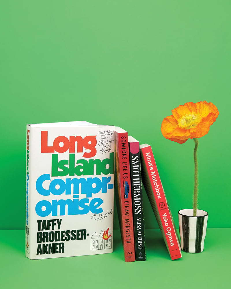 Four books (Long Island Compromise, Someone Like Us, Smothermoss, and Mina’s Matchbox) against a green backdrop, next to an orange flower in a striped vase.