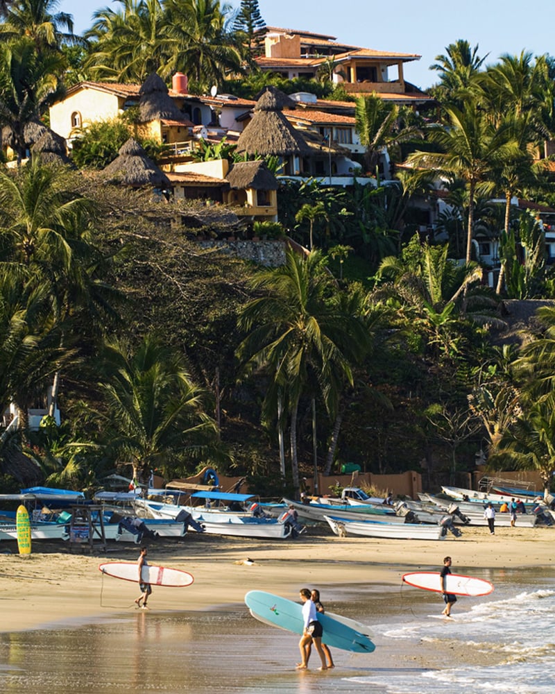 Surfers carry their boards across the sand at a beach in Sayulita on Mexico’s Riviera Nayarit.