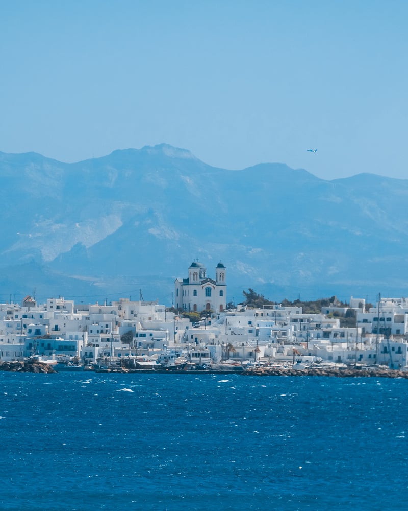 The coast of Páros, lined with white buildings, between the mountains and ocean.