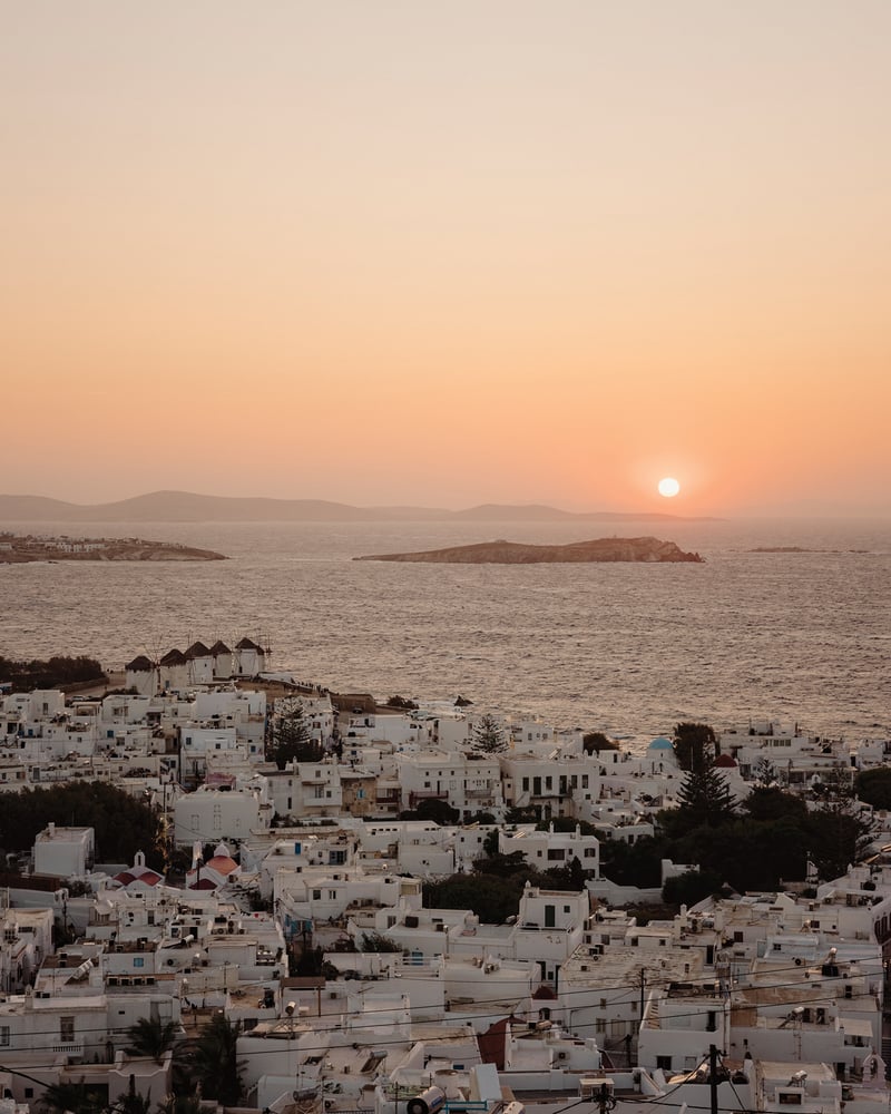 An orange sunset over the Mediterranean Sea and the white buildings of Mykonos.