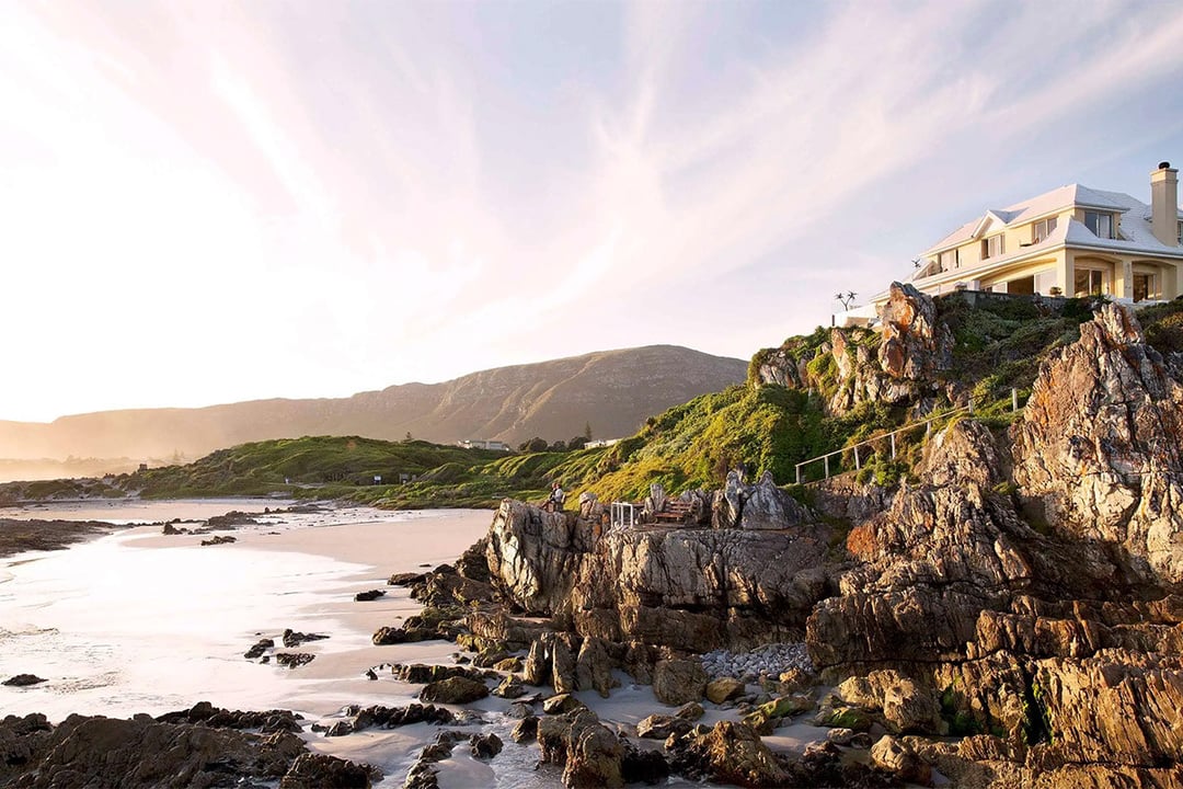 A house on top of a rocky bluff sits over the beach.