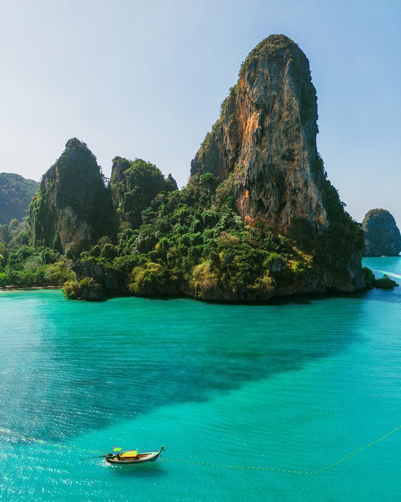 A karst islet in Phuket, with a longtail boat sailing past.