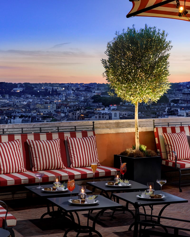 Red-and-white-striped patio chairs and black tables on Hotel de Russie’s rooftop terrace in Rome.