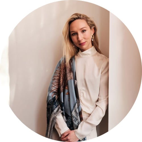 Sabina Savage smiles lightly at the camera, wearing white silk clothing and a blue printed silk scarf.