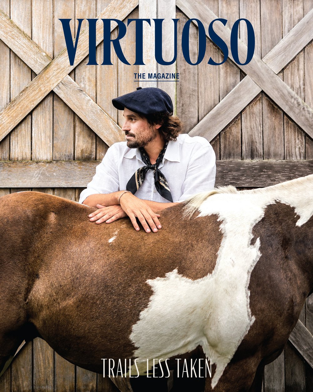 The September cover of Virtuoso, The Magazine shows a man wearing a white button-down, a scarf, and a beret, resting his forearms on a horse and looking off into the distance. The cover line reads “Trails Less Taken.”