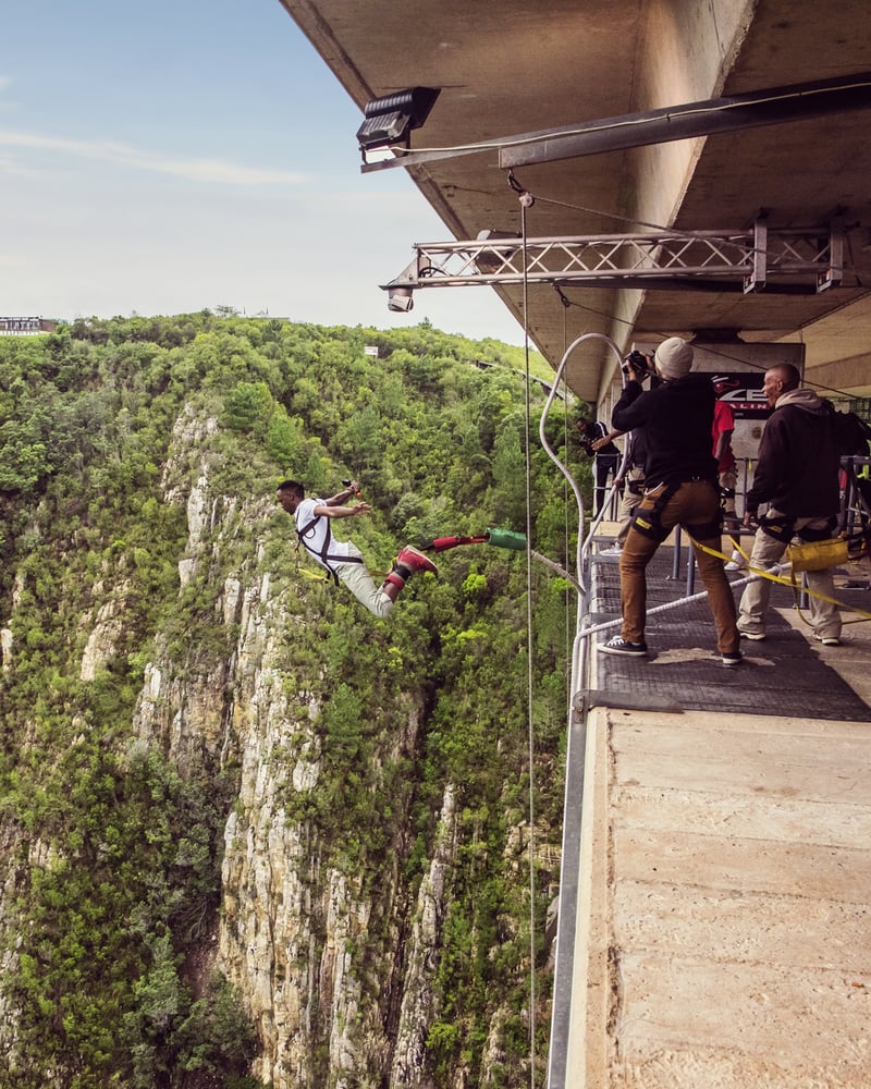 A person bungee jumps from Bloukrans Bridge in South Africa, with forested cliffs in the background.