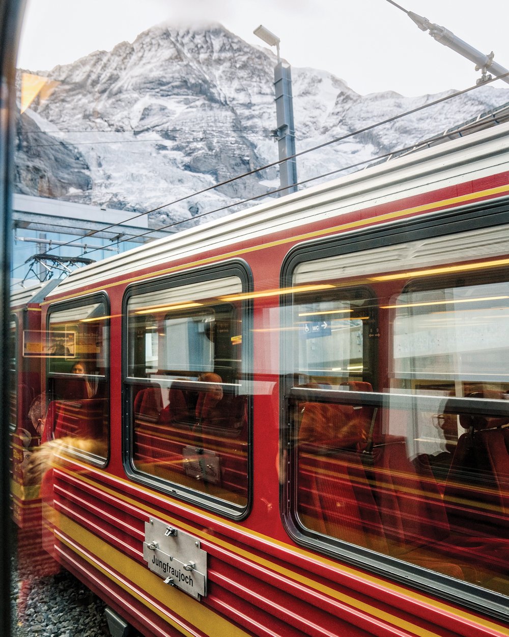 A red train emerges from a tunnel underneath the snowcapped Jungfrau Mountains.