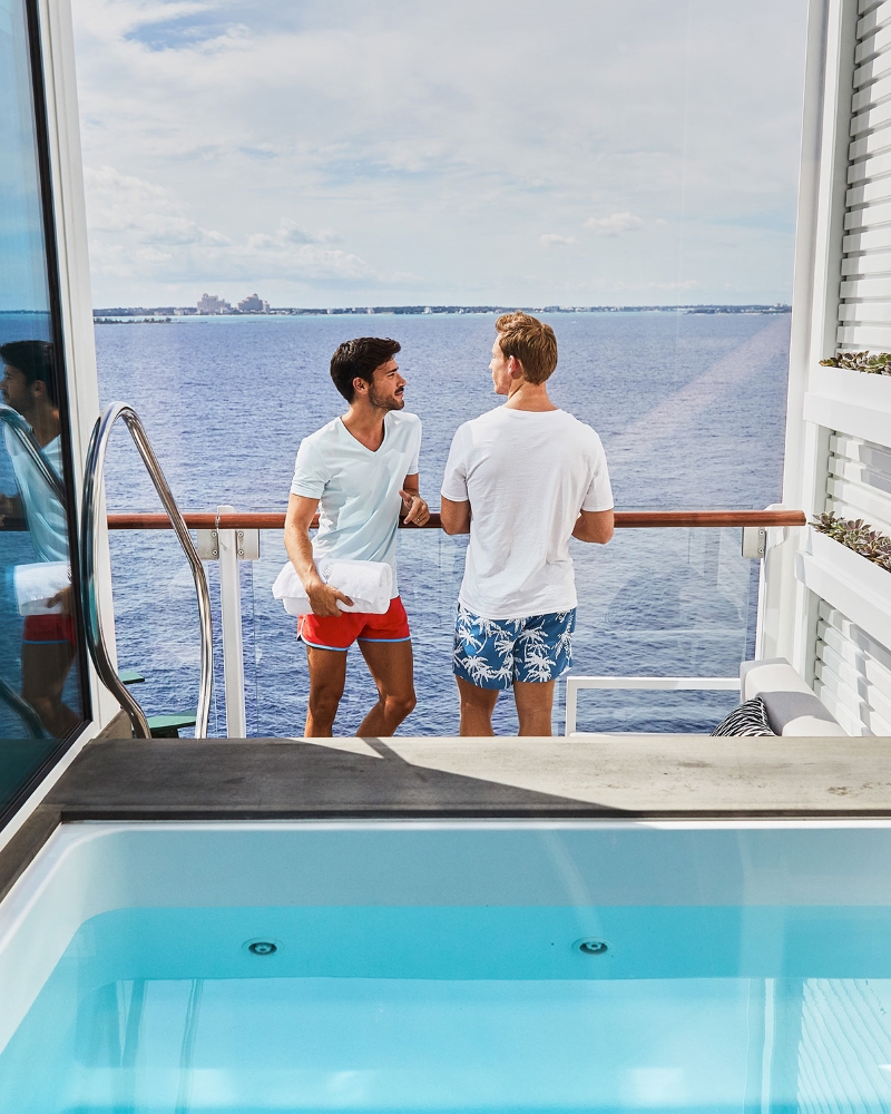 Two men stand together on a balcony aboard the Celebrity Edge.