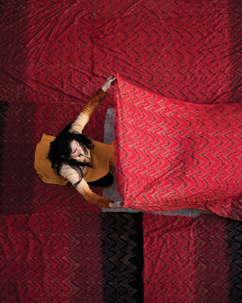An overhead shot of a woman shaking out a red, patterned bolt of fabric.