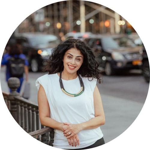 Writer Sarah Khan smiles at the camera, standing near a busy street.