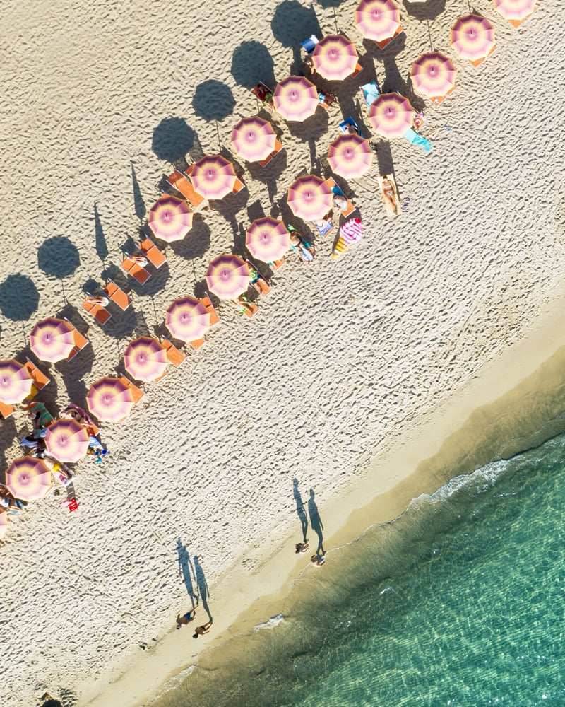 An overhead view of a beach lined with striped umbrellas.