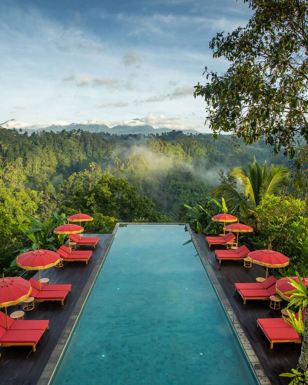 An infinity pool in the Balinese jungle, lined with crimson umbrellas and lounge chairs.