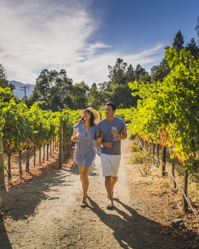 A couple walks through a California vineyard, wine in hand.